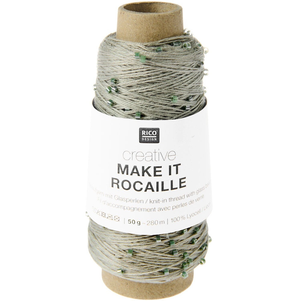 A spool of Rico Design Creative Make It Rocaille glass pearl knitting thread, featuring light gray and white thread with small green pearl accents, on a cardboard core with a white paper label.