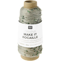 A spool of Rico Design Creative Make It Rocaille glass pearl knitting thread, featuring light gray and white thread with small green pearl accents, on a cardboard core with a white paper label.
