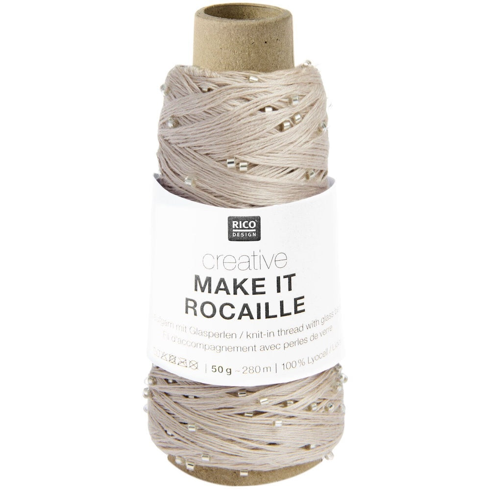 A spool of Rico Design Creative Make It Rocaille glassart knit-in thread, featuring light beige thread with tiny clear rhinestones, wound on a brown cardboard core with a white paper label.