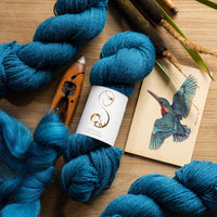 Blue yarn skeins with knitting needles and a bird illustration on a wooden surface